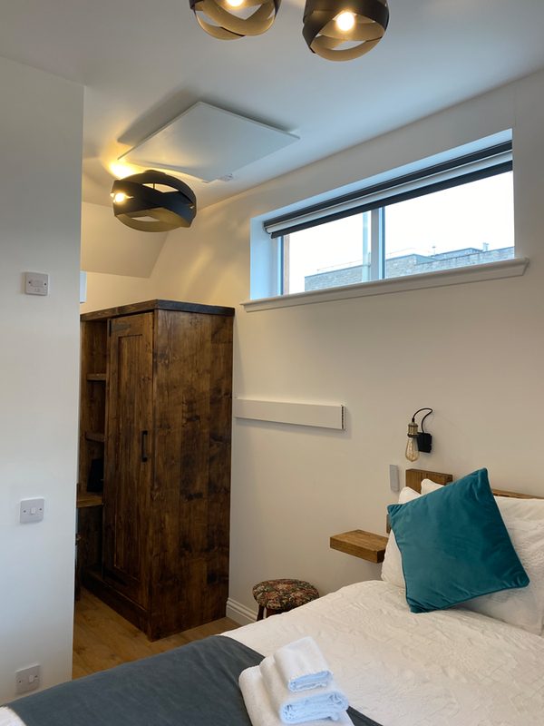 Bed beside the window, with a solid wooden door and teal cushions