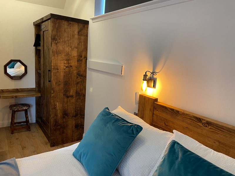 Bedroom with wooden bed frame, teal cushions and a wall lamp beside the wardrobe