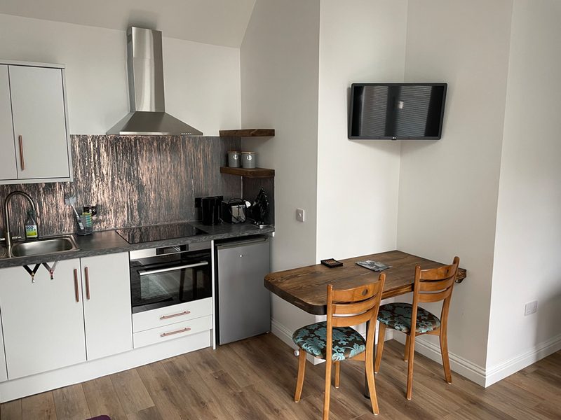 Wooden dining table for two beside the kitchen, with a wall-mounted television