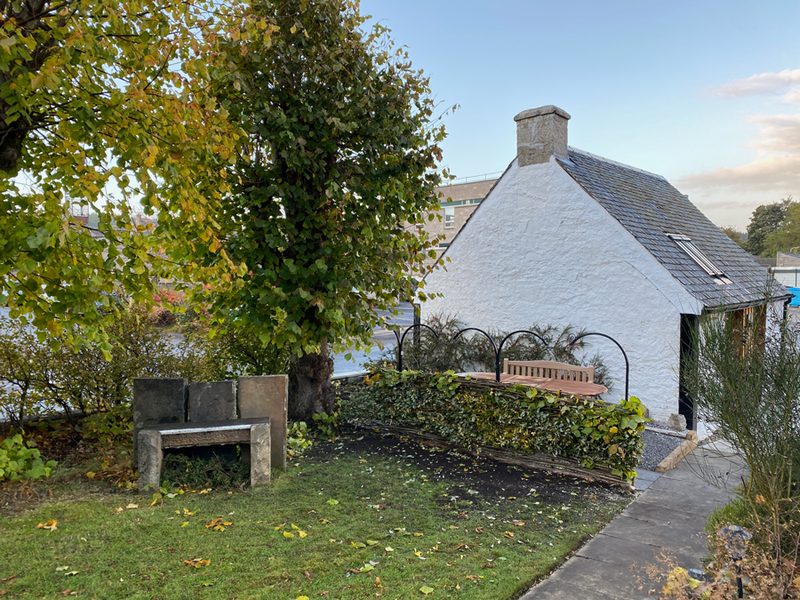 Lawn and garden bench in front of the cottage's white gable on an autumn morning
