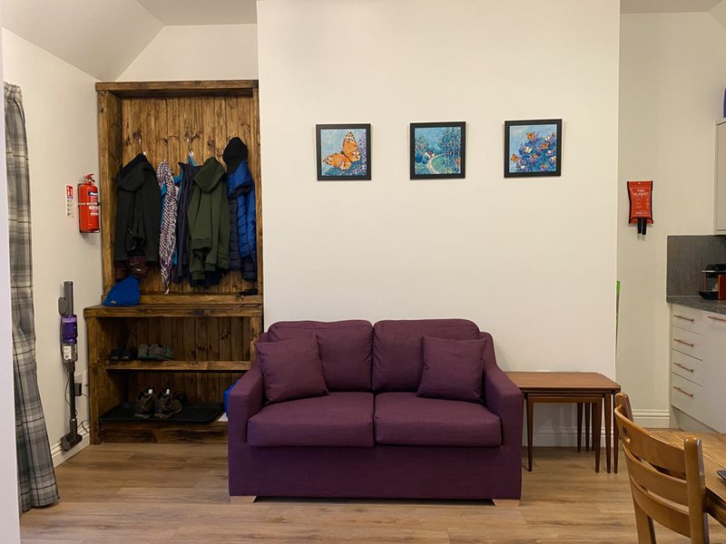 Entrance area with coat rack, plum sofa bed and three framed butterfly prints on the wall