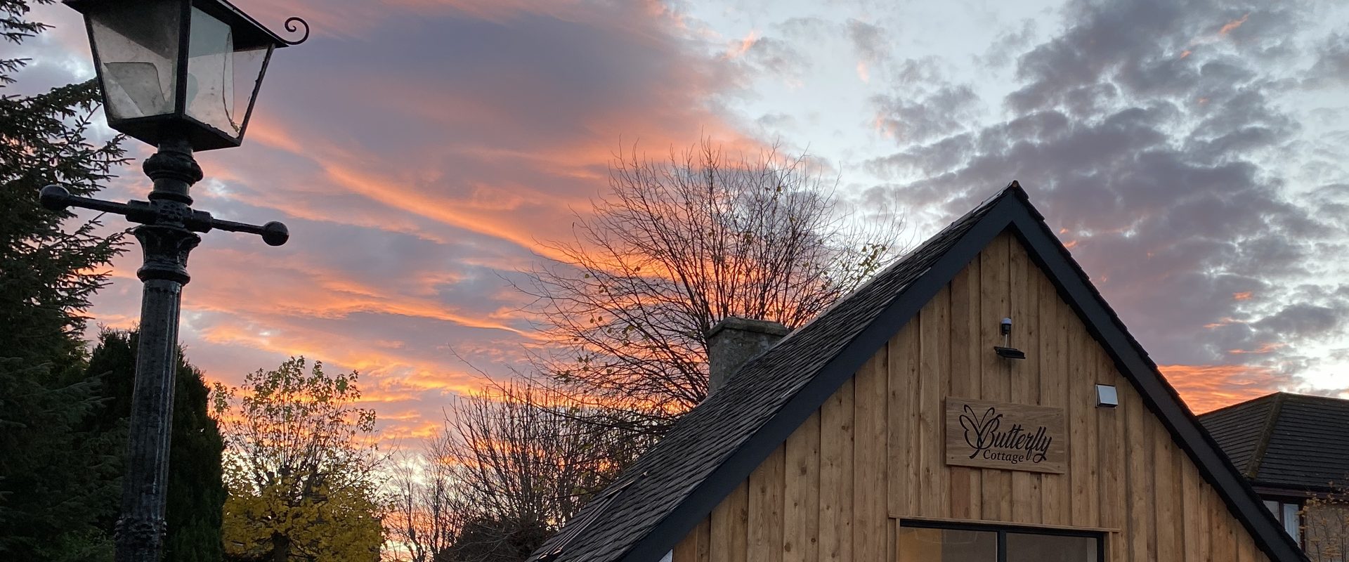 Butterfly Cottage at sunset, the larch-clad gable with its Butterfly Cottage sign under a sky streaked orange