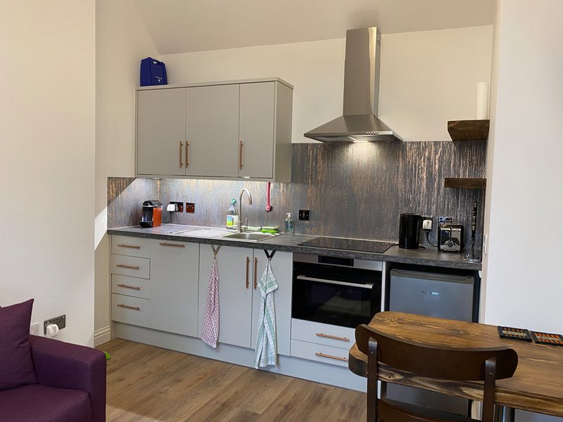 Kitchen with white units, ceramic hob, stainless extractor hood and dark patterned splashback