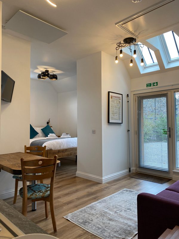 Open-plan living space seen from the kitchen, with dining table, bed area and garden doors